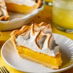 Lemon meringue pie with golden crust and fluffy meringue topping on a rustic wooden table.