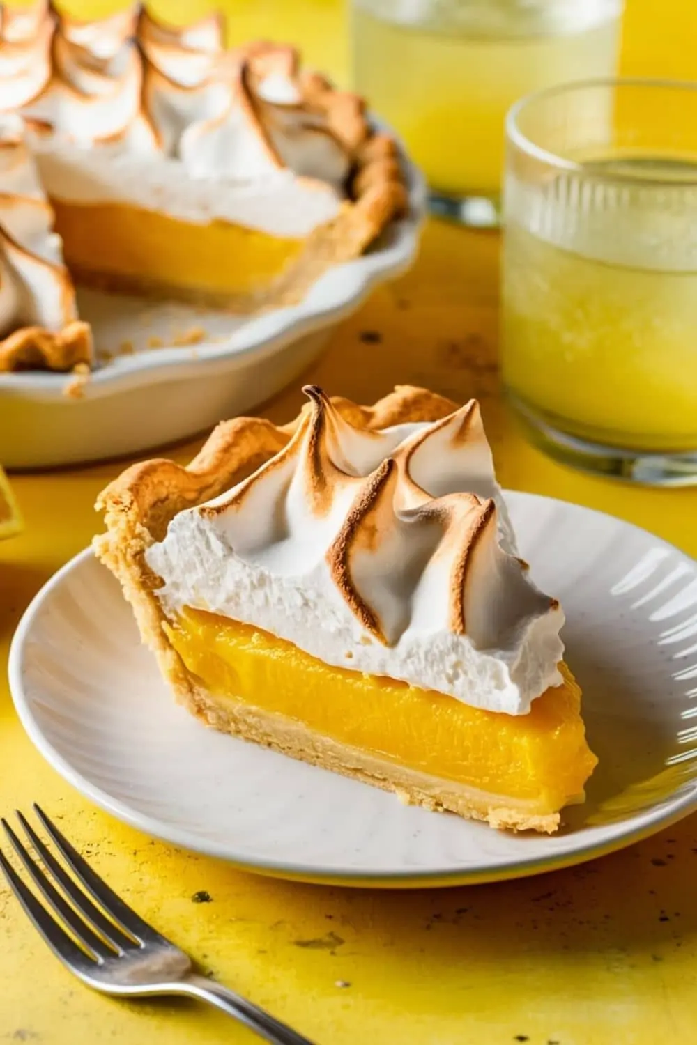 Lemon meringue pie with golden crust and fluffy meringue topping on a rustic wooden table.